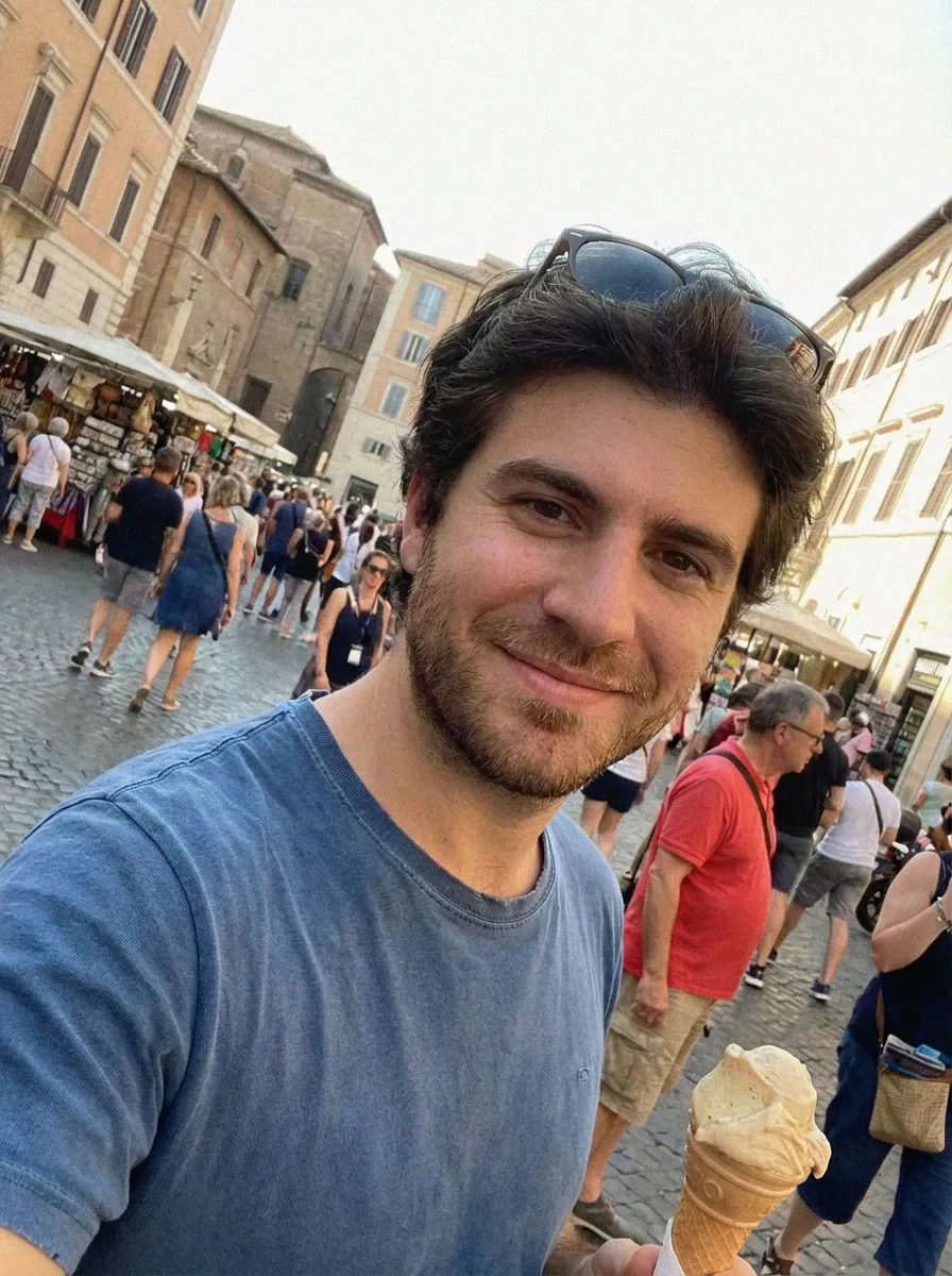 Travel selfie of a man in a blue T-shirt holding an ice cream in a busy European square